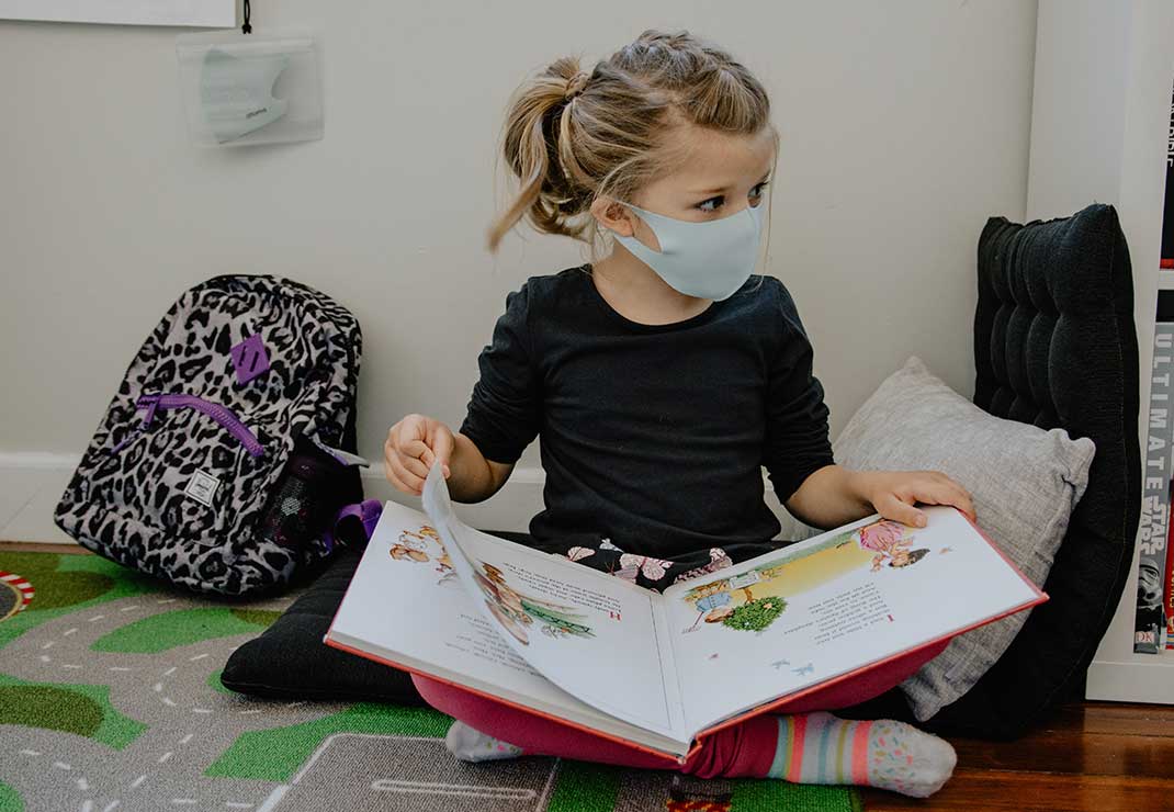 Young toddler girl reading a book as she sits on the floor.