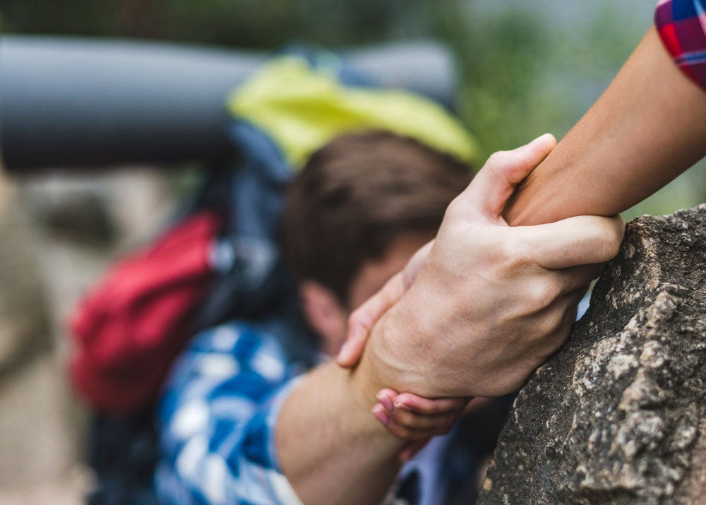 woman helping boyfriend to climb rock