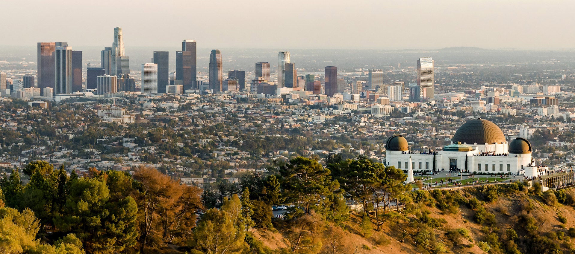 The Griffith Observatory sits in front of the Los Angeles skyline and city below the hill. 