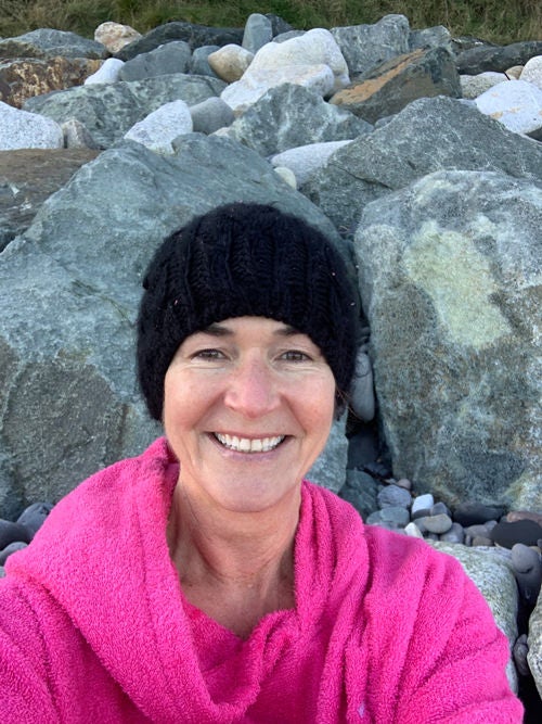 Ireland's general manager, Jane Dawson, smiling in a pink jacket and black fuzzy hat against a rocky background.