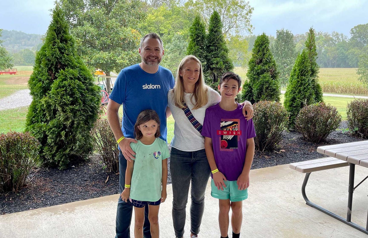 St. Louis general manager Saint Fults wearing a blue Slalom t shirt and jeans, standing alongside his wife in a white t shirt and jeans with their two children: a boy wearing a purple shirt and a girl wearing a mint-colored shirt.