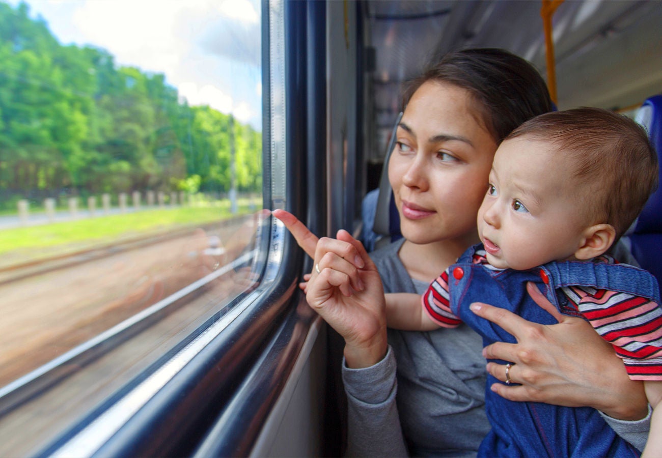 Woman holding a child on a train and looking out the window.