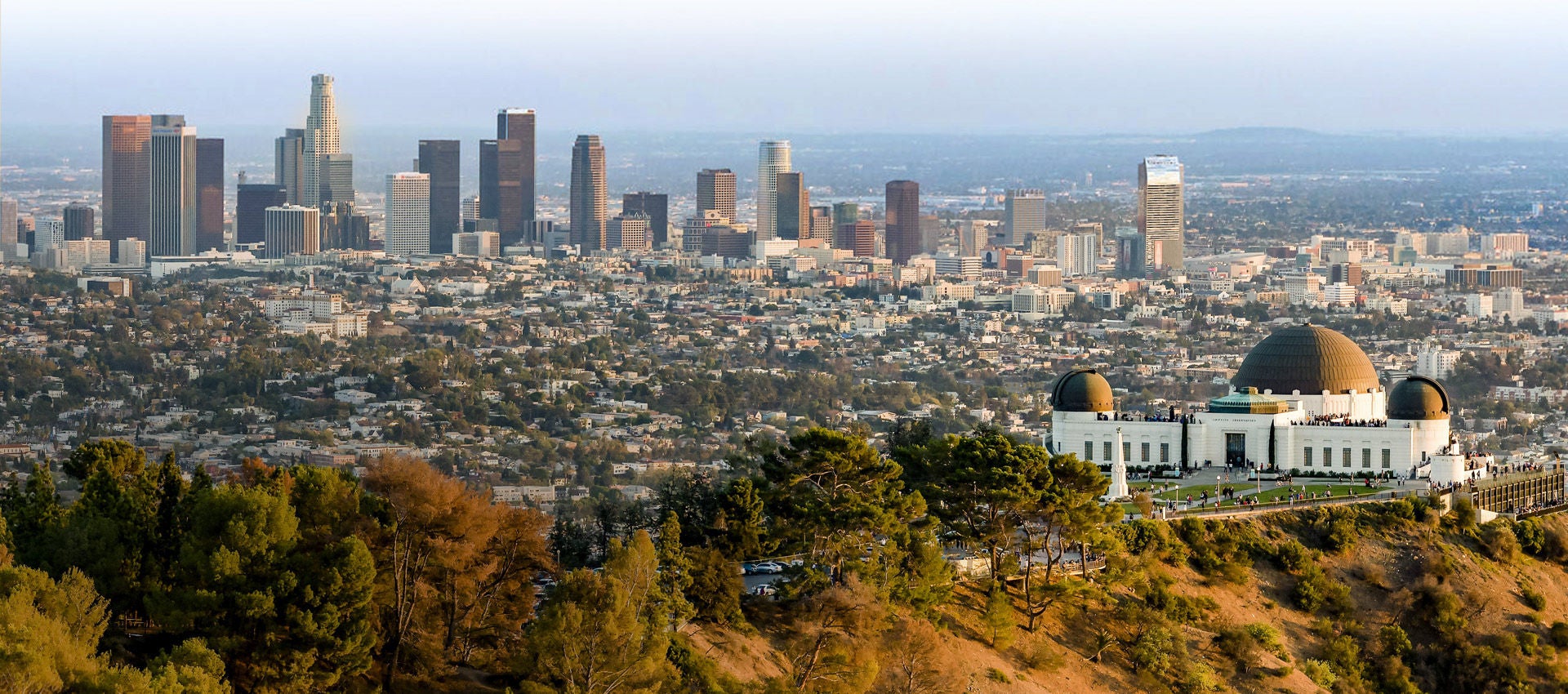 The Griffith Observatory sits in front of the Los Angeles skyline and city below the hill.