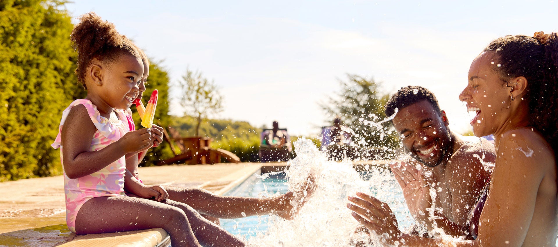 Family On Summer Holiday With Two Girls Eating Ice Lollies By Swimming Pool Splashing Parents placeholder