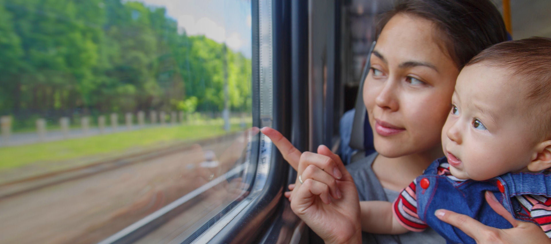 A mother and child look out the window of a train.