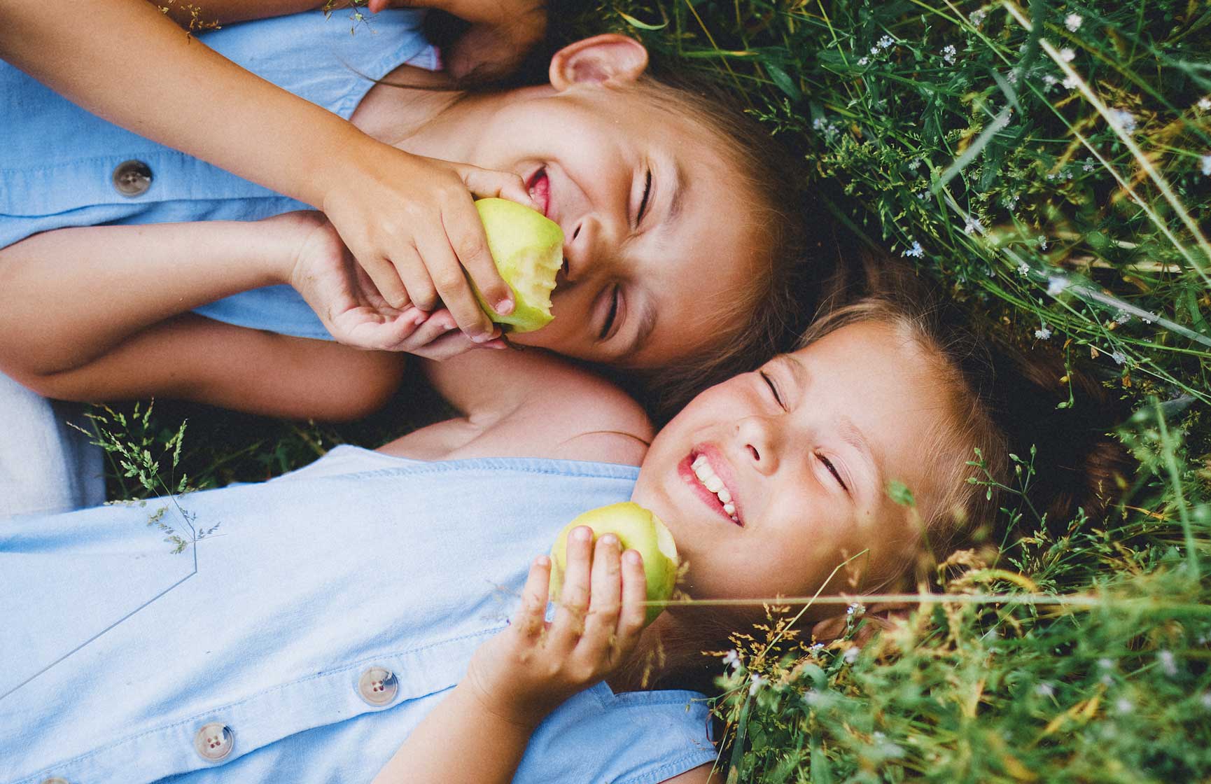 Two laughing children laying in the grass eating fruit