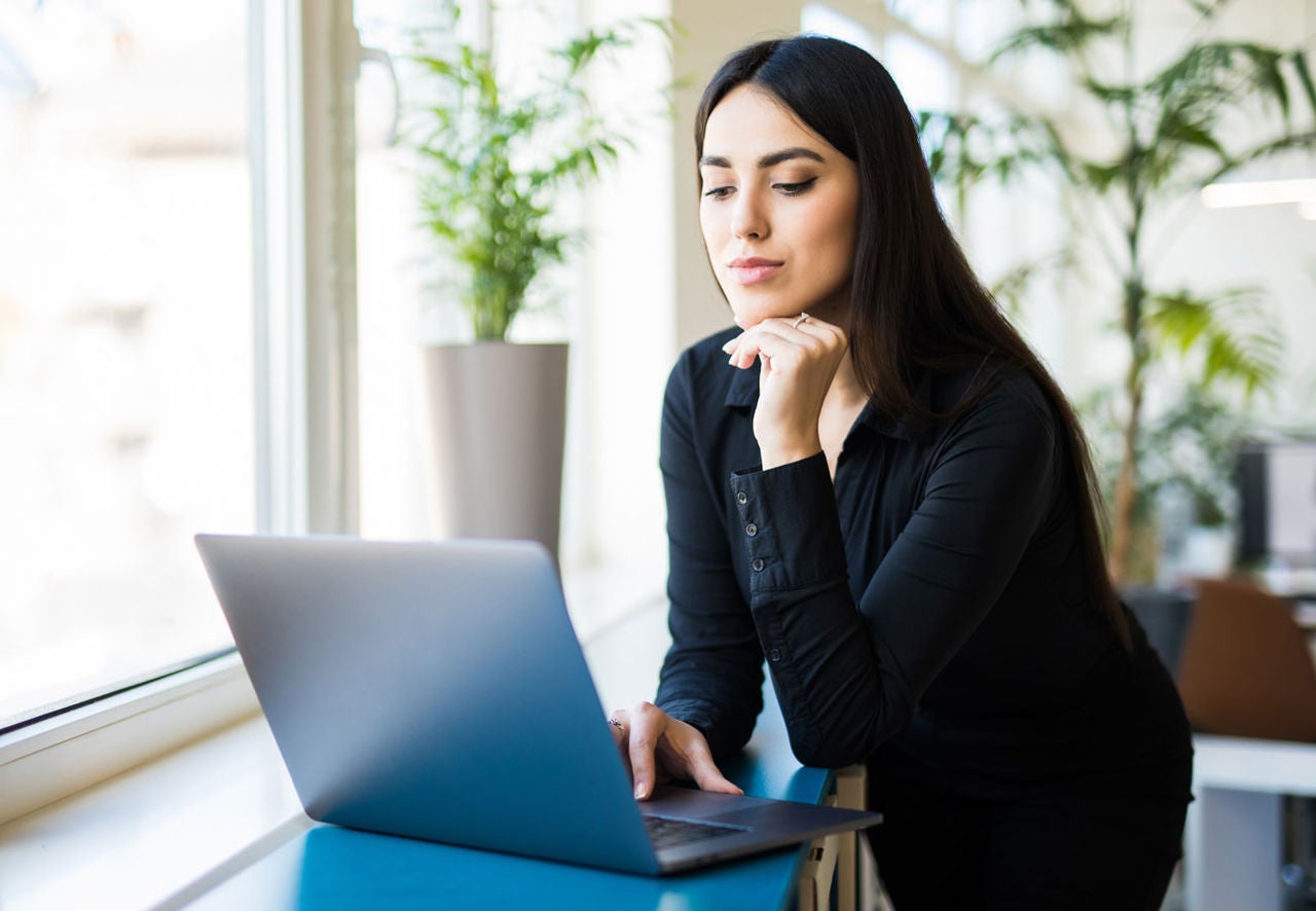 A woman works on a laptop in a sun filled office.