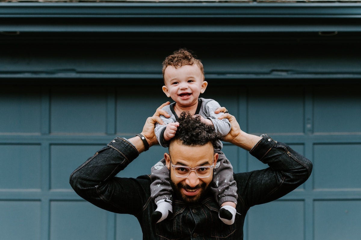 Child on parent's shoulders in front of garage.