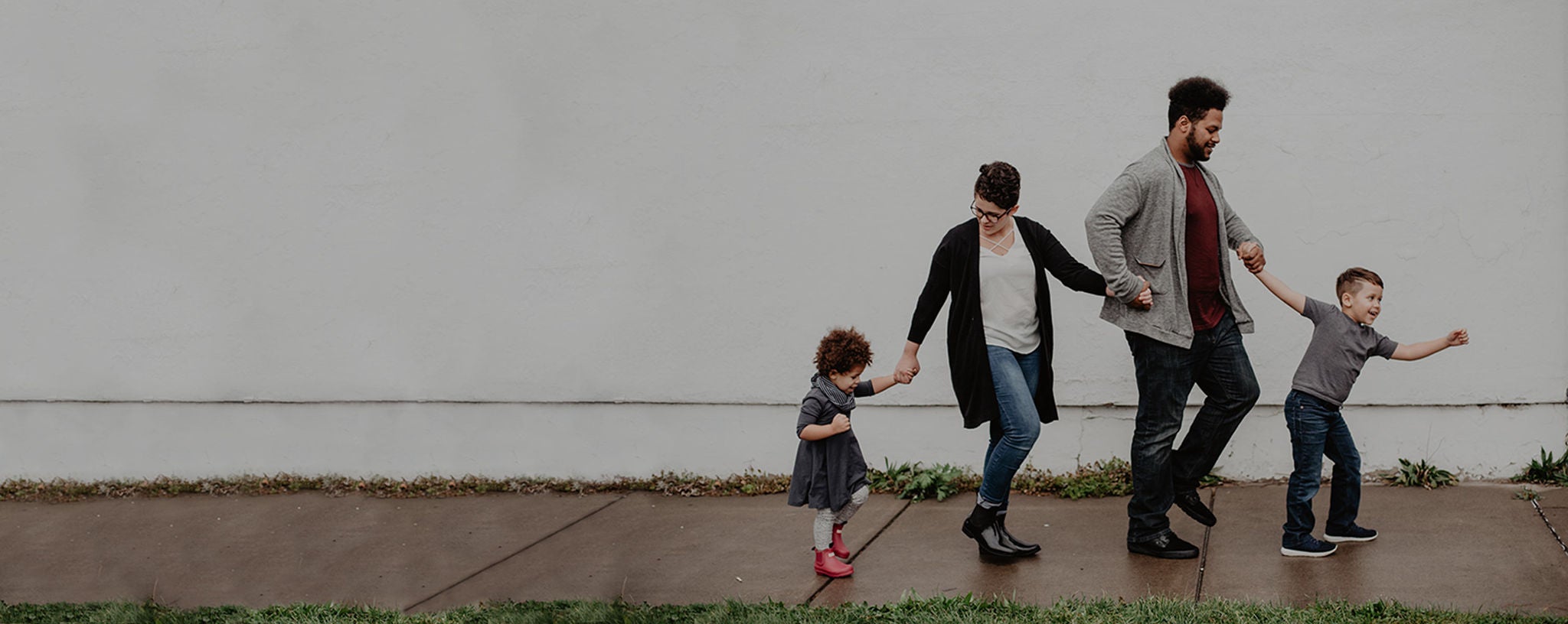 A family of four with son leading the way as their walking on the sidewalk.