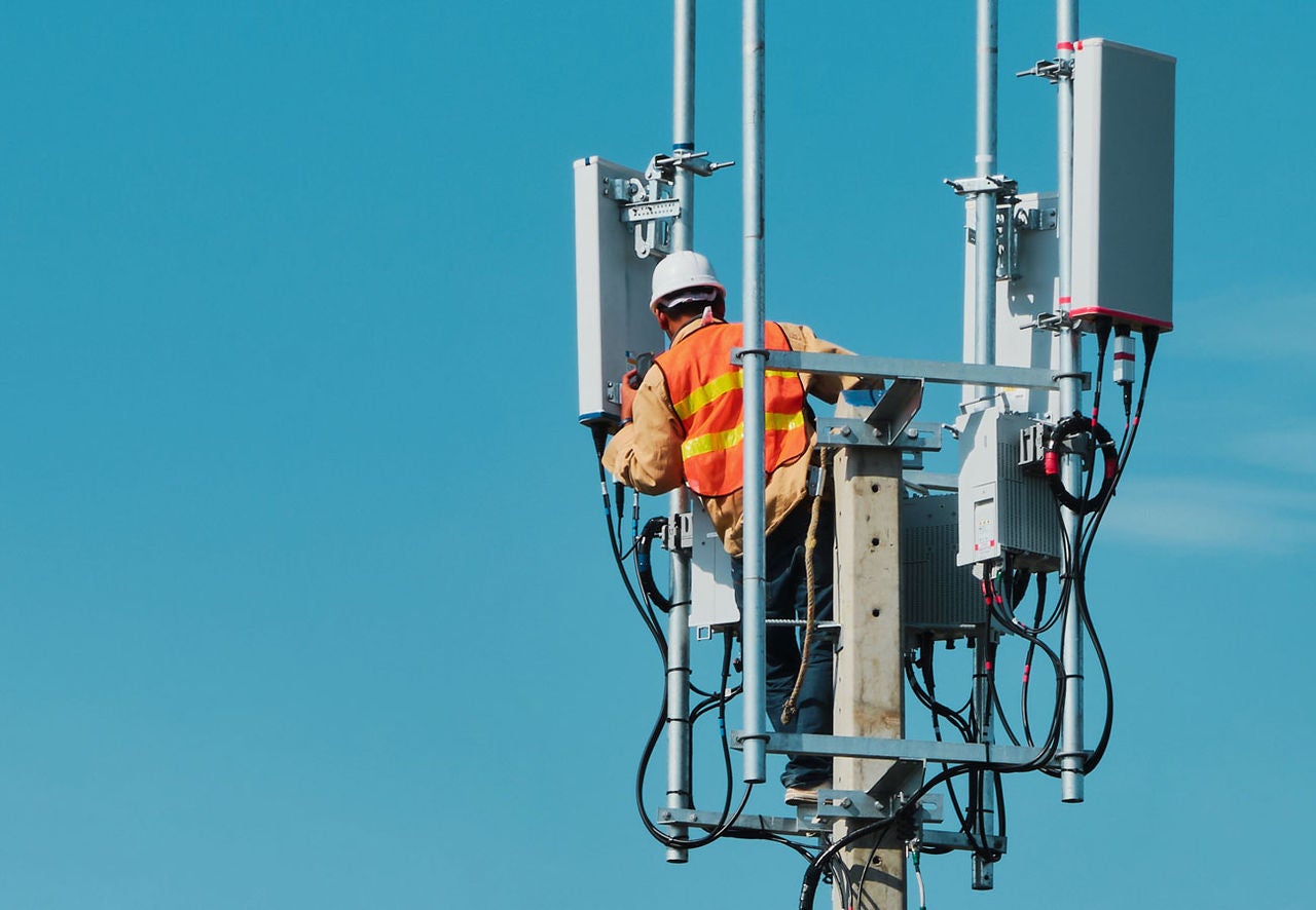 A person perforamce work on a communications tower on a sunny day.