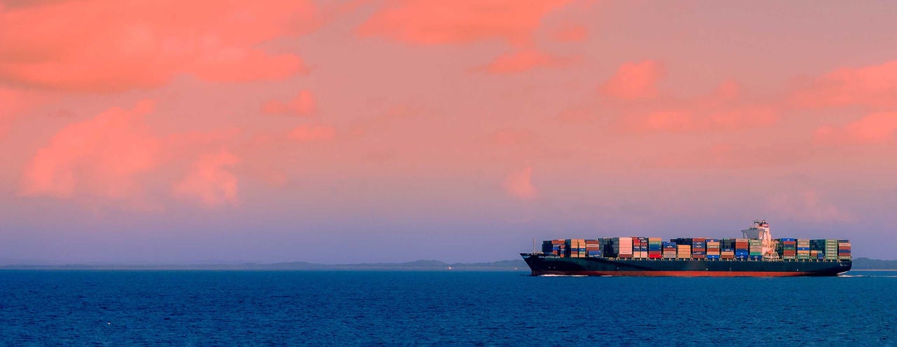 Sunset skies in background as a cargo ship is on the ocean.