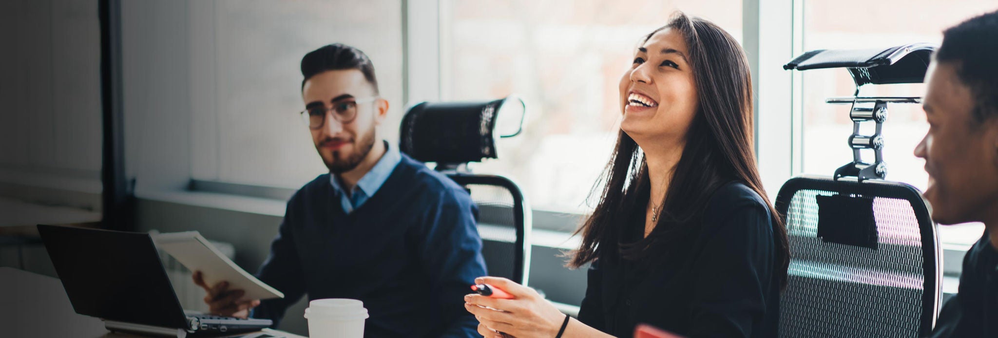 Positive diverse team of professionals dressed in formal wear laughing while collaborating on common project during briefing in modern office. Cheerful employees having fun during business meeting.