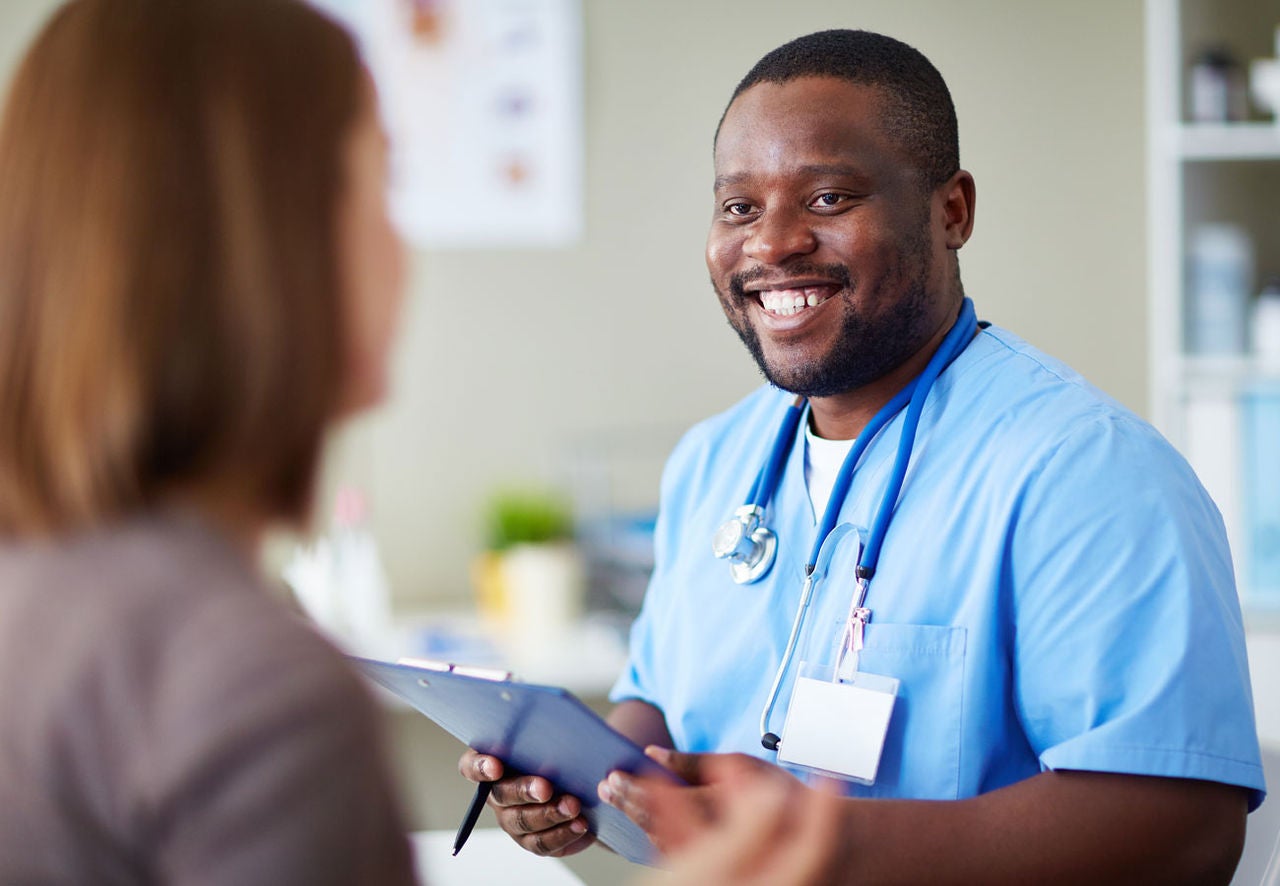 Healthcare practitioner in blue scrubs is holding a clipboard, smiling at patient