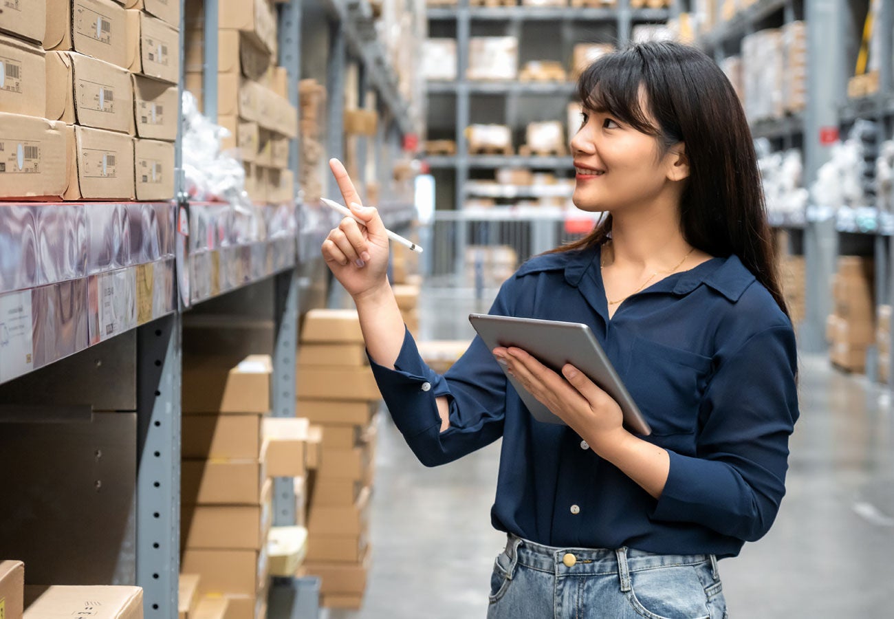 A woman takes inventory in a warehouse while holding a tablet. 