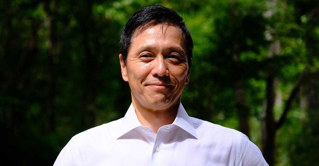 Headshot of Japan's general manager, Ko Asami, wearing a white shirt against a forested backdrop.