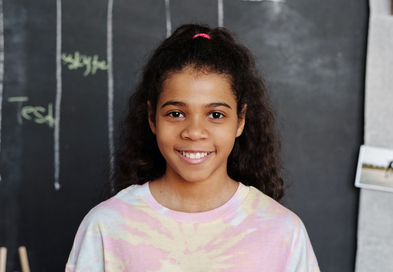 A smiling young student stands near a chalkboard. 
