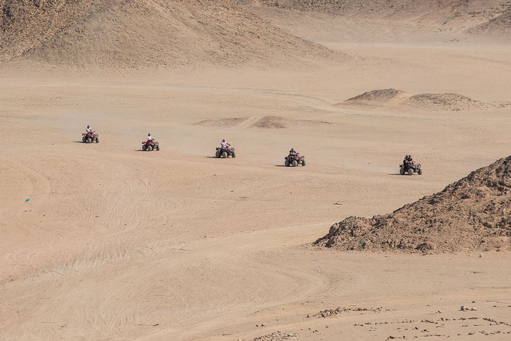 Five ATVs traversing the sand dunes of a desert.