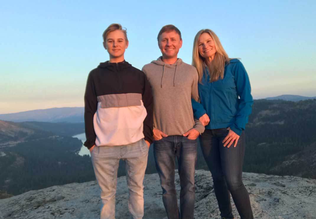 NorCal general manager Sarah Duffy wearing a blue jacket and jeans, standing on top of a mountain alongside her husband in a gray sweater and her son in a black, white, and gray sweatshirt.