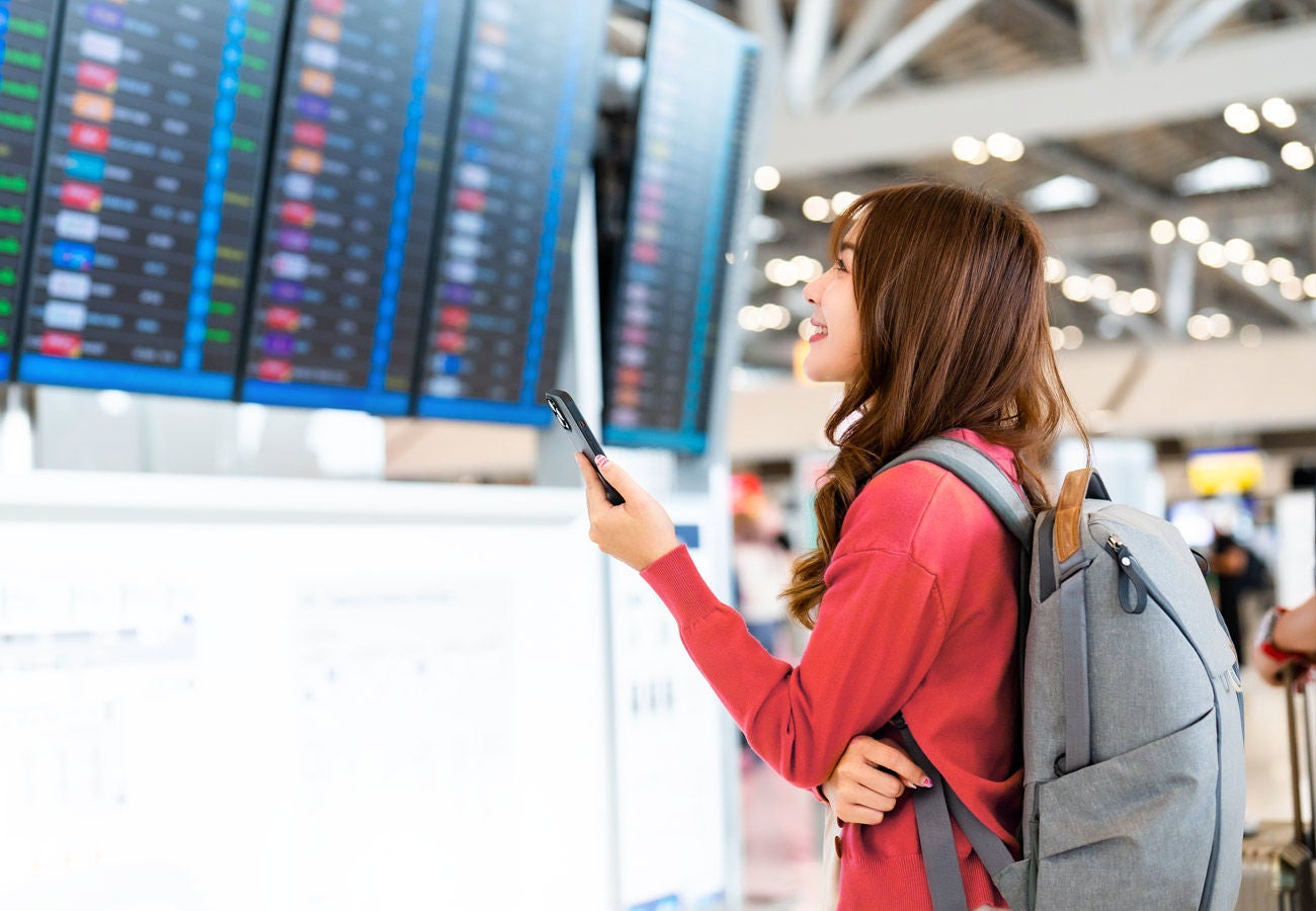 A woman looks at departure information screens in a large airport.