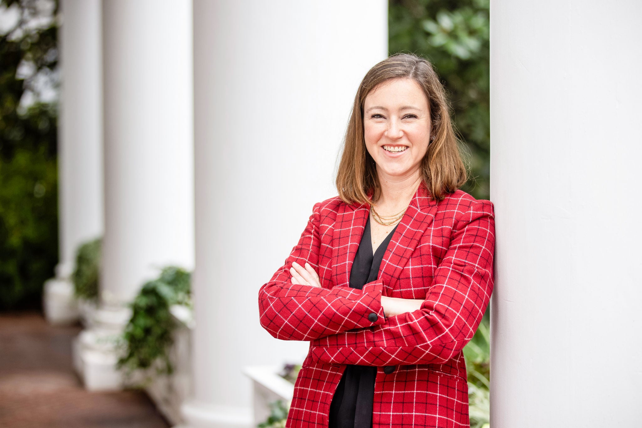 Headshot of Charlotte general manager, Kelly Adkisson, wearing a red plaid blazer and leaning against a white column, smiling.