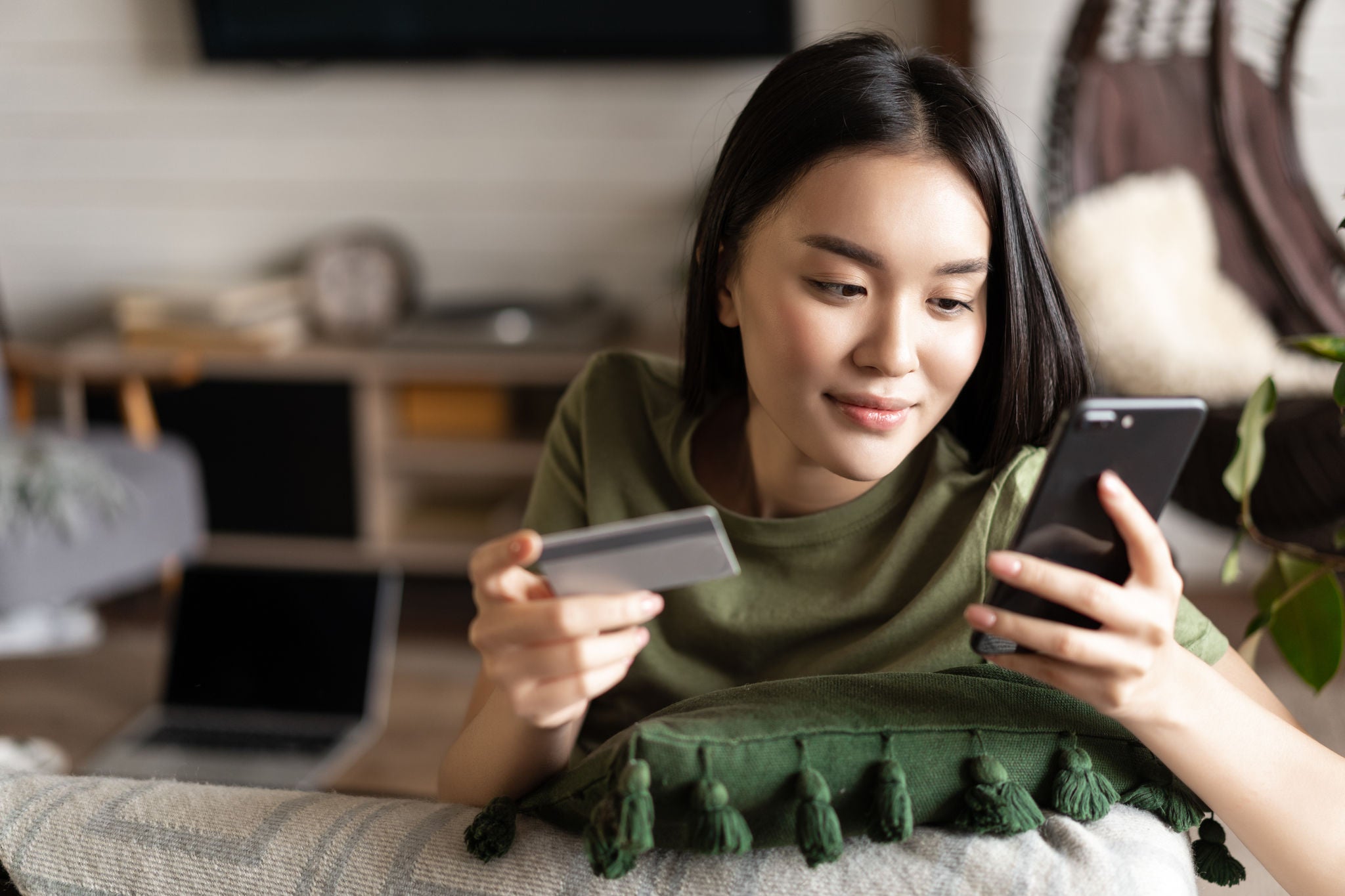 Young asian woman buying from online shop, using mobile phone and credit card, shopping from home.