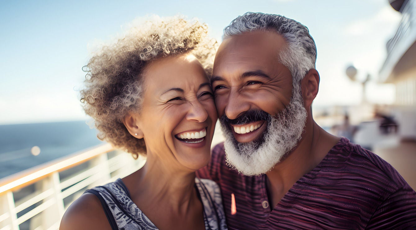 A couple smiles as they stand outside on a sunny day while onboard a cruise ship.