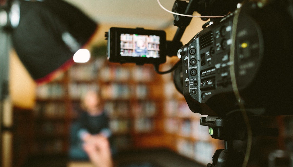 Camera filming with person in chair in TV studio.