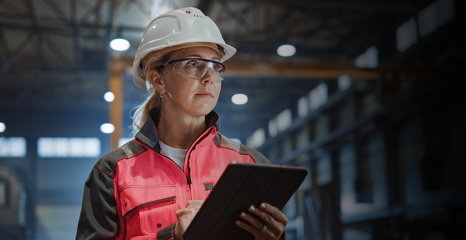 Professional Heavy Industry Engineer/Worker Wearing Safety Uniform and Hard Hat Uses Tablet Computer. Serious Successful Female Industrial Specialist Walking in a Metal Manufacture Warehouse.