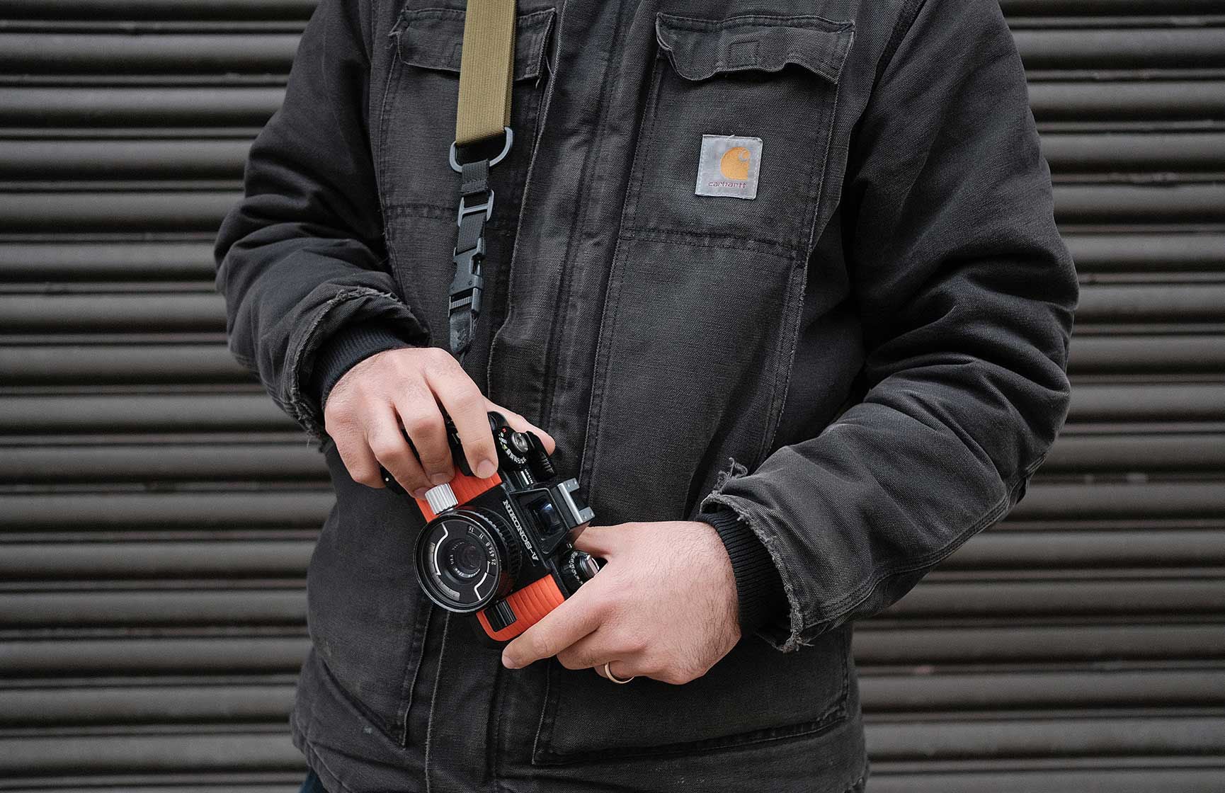 Close up photo of a man holding a camera wearing a Carhartt jacket.