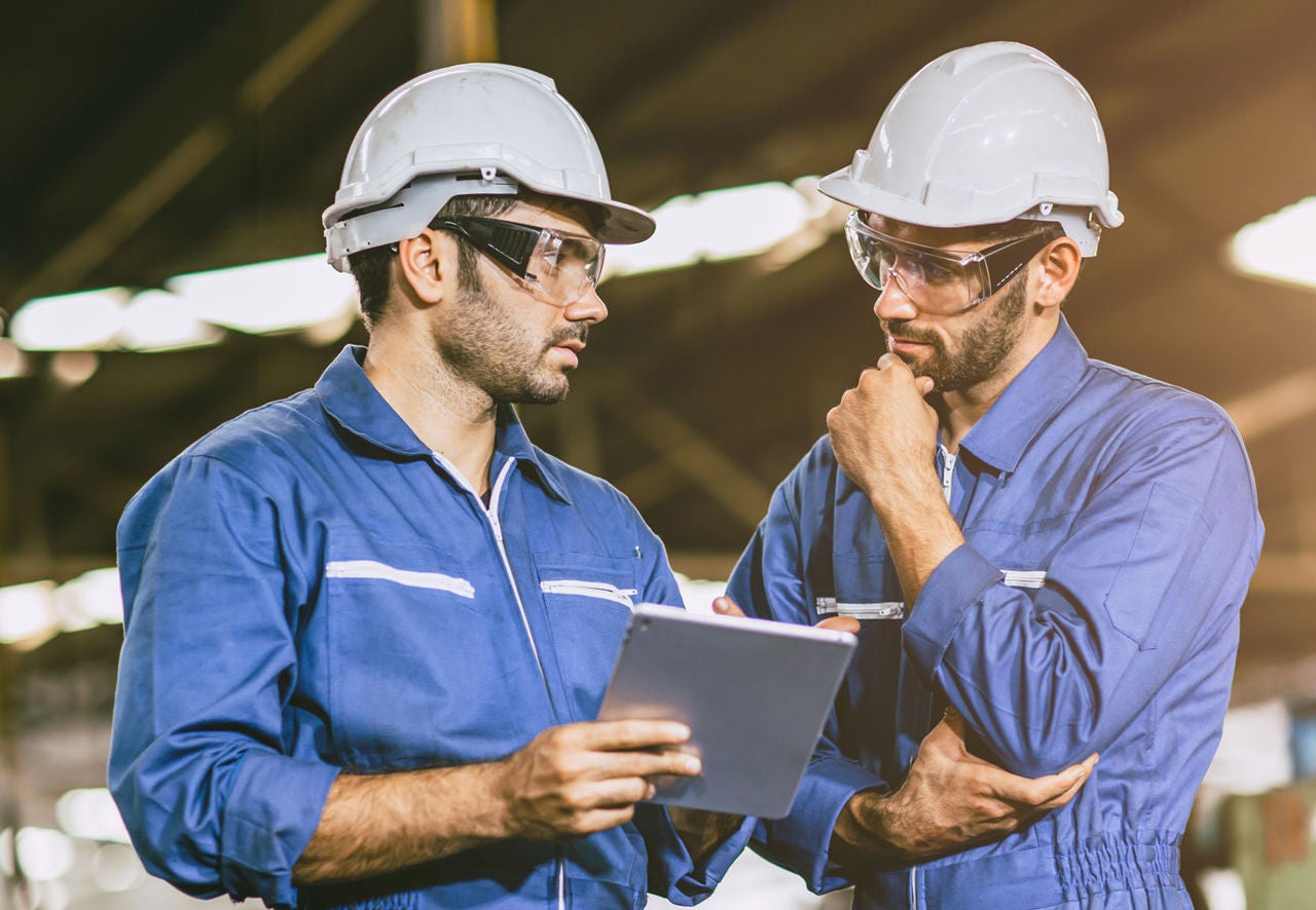 Two men work together to solve a problem in an industrial facility.