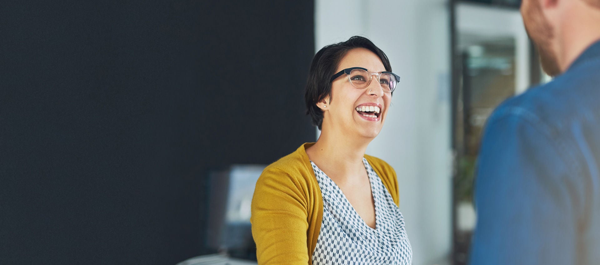 A woman laughs with a colleague in the office of a company.