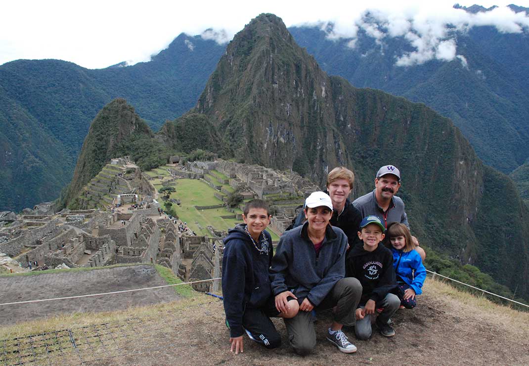 Seattle general manager Jila Javdani wearing white hat and dark clothes, crouched in front of Machu Picchu in Peru with her husband, three sons, and young daughter.