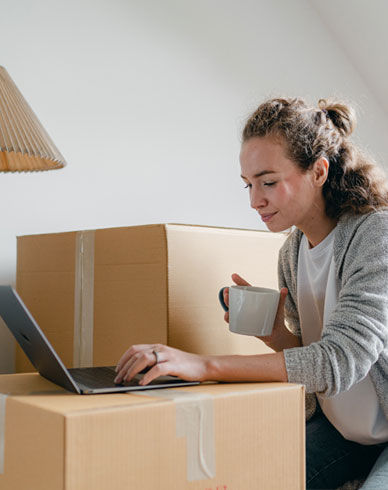Woman working on laptop holding a cup of coffee while packing